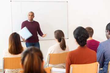 Hispanic lecturer offering product for sale near board to multinational people