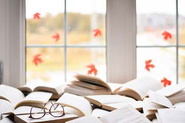 Multiple open books on a table by a window with autumn leaves