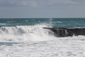 Waves are crashing on a group of stones.