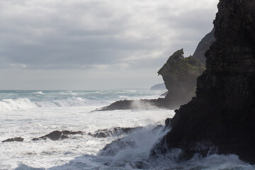 Fototapeta na wymiar Marine landscape with an inclined rock, waves and cloudy sky on background, West Beach near Auckland, New Zealand.