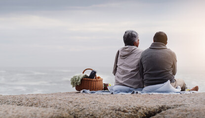 Were having a picnic by the beach today. Rearview shot of an affectionate senior couple having a...