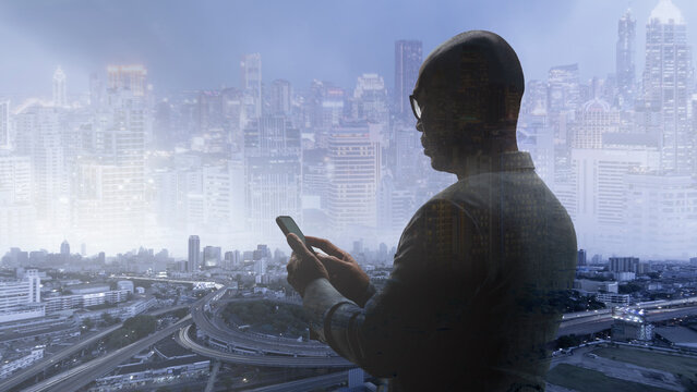 Panorama of business man standing over large windows using smartphone with city background. The image creates multiple layers by photoshop.