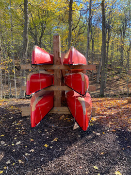 Canots rouges sur un support en bois en for&ecirc;t &agrave; l'automne. Location d'embarcation nautique, cano&euml; de rivi&egrave;re, rabaska dans un parc national. Centre de plein air et de camping.