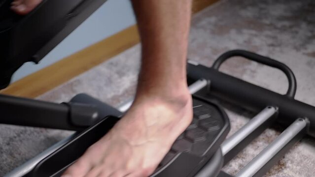 Barefoot Male Feet Pedaling on Elliptical Cross Trainer Simulator at Home. Playing sports, fitness during quarantine. Leg movement on adjustable foot pedals. Cardio cross-trainer. Slow motion.