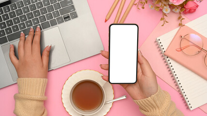 Female hand holding a smartphone and searching on laptop