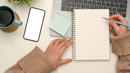 Top view, Female in comfy sweater writing her diary in minimal workspace.