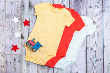 White, yellow and red cotton bodysuit with children's toy. Clothes for newborns on a gray...