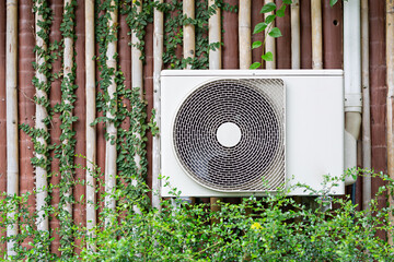 The air conditioner is mounted on the wall with the trees of the building with the garden in the...
