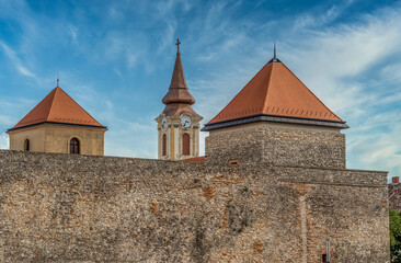 Fototapeta na wymiar The towers of Varpalota Hungary. Two square shape medieval castle tower of the Thury castle with red roof and the baroque clock tower of the municipal catholic church