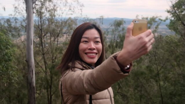 Young smiling Asian woman takes phone selfie in natural environment