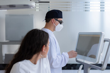 Focus on male dentist touching a screen while his female patient is waiting for him. Dental clinic concept