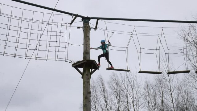 Girl walking across planks on ropes on a high wire adventure obstacle course