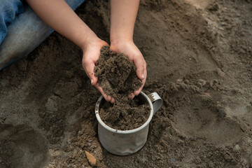 Children playing with sand in the sandbox in the schoolyard. Activity for fine motor skills, fill an aluminum cup with sand, enjoy outdoors