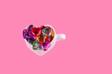 Multicolored hearts in a heart-shaped mug on a pink background