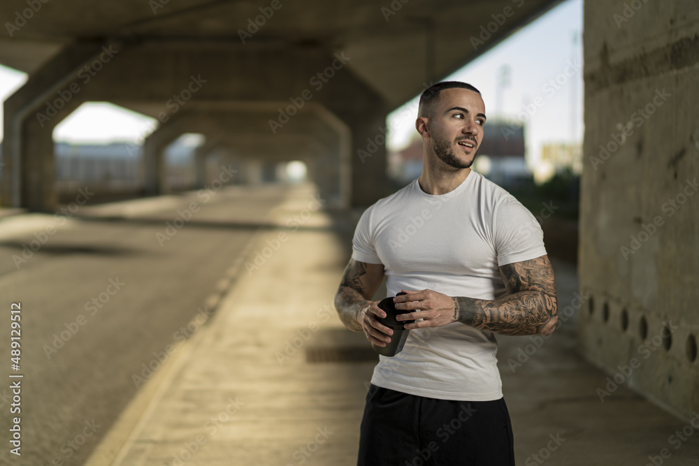 Sticker cheerful muscular european guy with cool tattoos posing on a sunny road