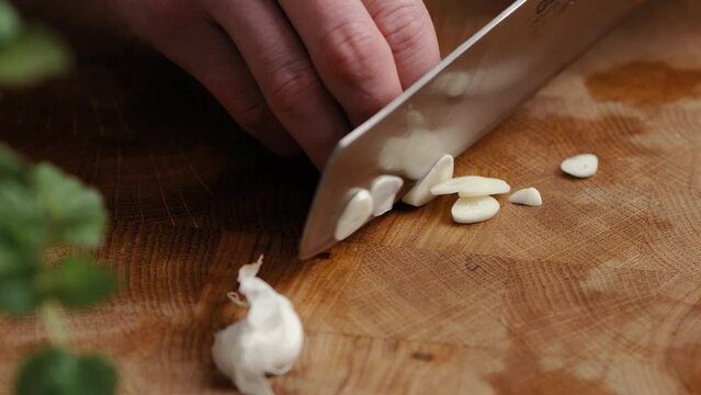 Male chef sliceing garlic in thin slices in the kitchen on a wooden cutting board in the kitchen. Close Up Zoom In