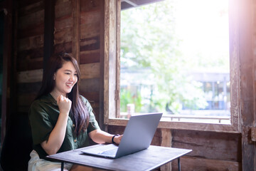 Happy successful business of asian freelance people business female expressed confidence embolden working with laptop computer sitting with coffee cup beside the window of a wooden house background