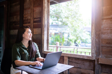 Happy of asian freelance people business female  wearing brownish green dress stylish hipster casual working with laptop computer with coffee cup beside the window of a wooden house background