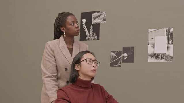 Medium slowmo portrait of young Asian man with disability and African-American woman carrying his wheelchair smiling at camera while visiting contemporary art gallery