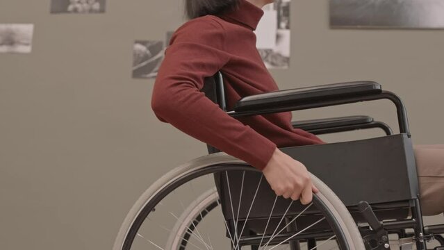 Cropped slowmo shot of unrecognizable wheelchair user at exhibition in contemporary art gallery