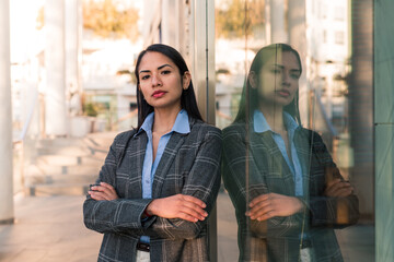 Young business woman with with a defiant look and her arms crossed leaning against an office building.