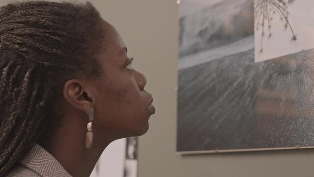 Slowmo close-up of young African-American woman standing close to abstract picture on wall of contemporary art gallery
