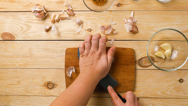 Close-up of women's hands crushing garlic cloves with a knife. Top view. Healthy and wholesome food every day.