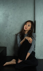 Fototapeta premium Young woman sitting sad at wall, depression emotion, looking above space in dark room, Portrait of young beautiful woman or female or girl sitting expression depression emotional alone