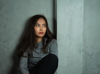 Young woman sitting sad against wall, depression emotion, looking above space in dark room, Portrait of young beautiful woman or female or girl sitting expression depression emotional alone