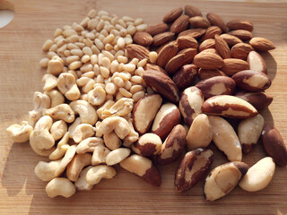 Raw nuts on the wooden board, brazil nuts, almond, pine nuts and cashew.