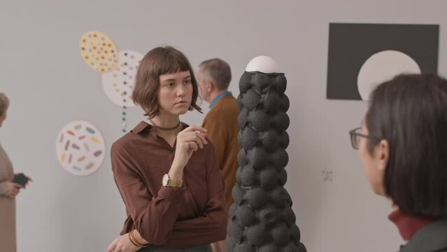 Medium slowmo shot of diverse couple of young people discussing and examining conceptual art object during exhibition in modern art museum