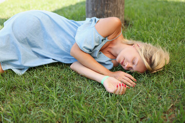 A woman in a blue dress sleeps on the green grass, close-up