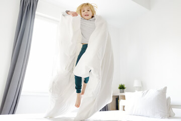 Happy little boy in pajamas jumps on his parents bed in the morning. Mischievous, naughty and playful active child.