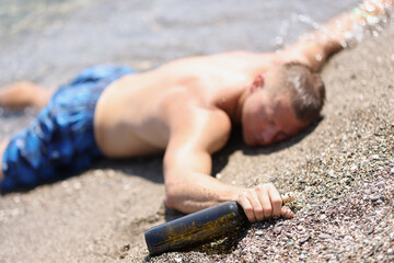 A drunk man with a bottle lies on the wet sand, blurry