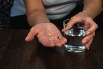 A woman holds a pill and a glass of water in her palms. Taking medication.