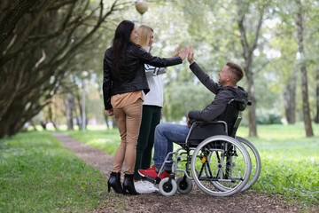 Fototapeta premium Young womens high five to men on a wheelchair in the park