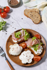 Easter breakfast or brunch. Delicious breakfast or snack - poached egg and cream cheese toast whole grain rye bread, prosciutto, arugula on a marble tabletop.