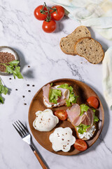 Easter breakfast or brunch. Delicious breakfast or snack - poached egg and cream cheese toast whole grain rye bread, prosciutto, arugula on a marble tabletop. Top view flat lay.