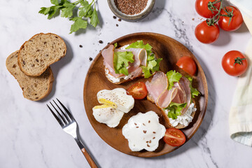 Easter breakfast or brunch. Delicious breakfast or snack - poached egg and cream cheese toast whole grain rye bread, prosciutto, arugula on a marble tabletop. Top view flat lay.
