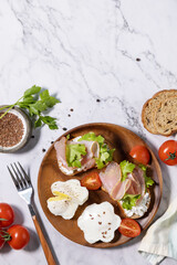 Easter breakfast or brunch. Delicious breakfast or snack - poached egg and cream cheese toast whole grain rye bread, prosciutto, arugula on a marble tabletop. Top view flat lay. Copy space.