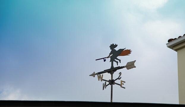 A weathervane on the roof of a house on a sunny blue sky day