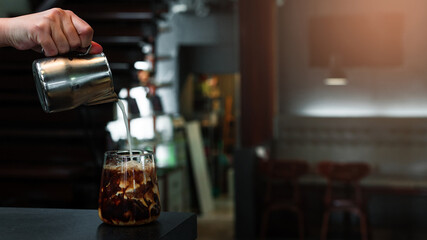 Barista pouring milk into a glass of iced coffee