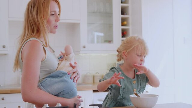 Girl at kitchen counter eating breakfast watching mobile phone whilst mother holds baby - shot in slow motion