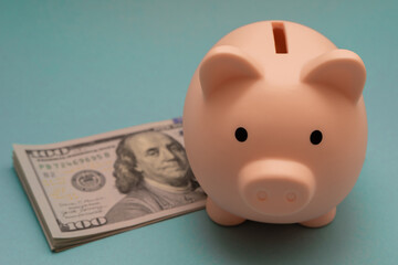 Pink piggy bank and a stack of dollars on a blue background close-up. Saving and accumulating money, financial security, budget planning and investment.