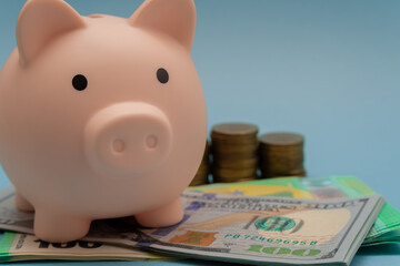 Pink piggy bank and a stack of dollars, euros and coins on a blue background close-up. Saving and accumulating money, financial security, budget planning and investment.