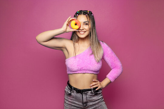 Fashion portrait of a happy trendy modern pretty young woman with tasty donuts cake on colorful bright pink banner background