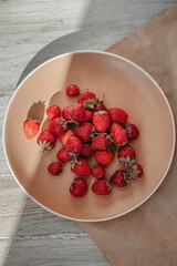 Garden strawberries on a beige plate on which a sunbeam falls.