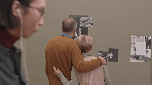 Rear-view medium slowmo shot of mature Caucasian couple and other tourists visiting photo exhibition in contemporary art gallery