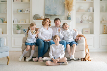 Portrait large family spending time together at home. They are happily sitting in the living room on the couch in a modern light interior. Caucasian parents with children spend time on weekends