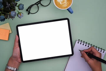 Woman hand holding digital tablet and writing information on notepad.